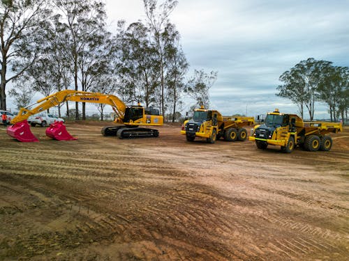 Earthmoving machines standing idle on dirt with trees in background